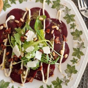 A plate filled with a vegetarian carpaccio of beetroot with many toppings.