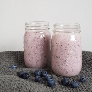 A blueberry pineapple smoothie in a Mason Jar, with fresh blueberries in front.