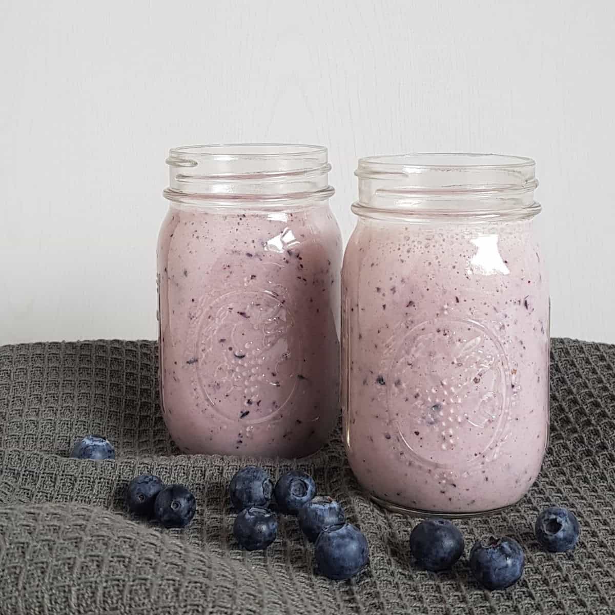 A blueberry pineapple smoothie in a Mason Jar, with fresh blueberries in front.