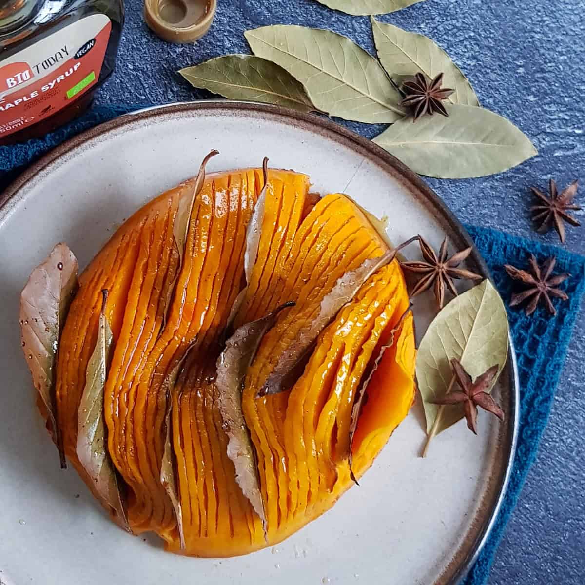 A halved roasted pumpkin with a maple syrup glaze, inserted with bay leaves.