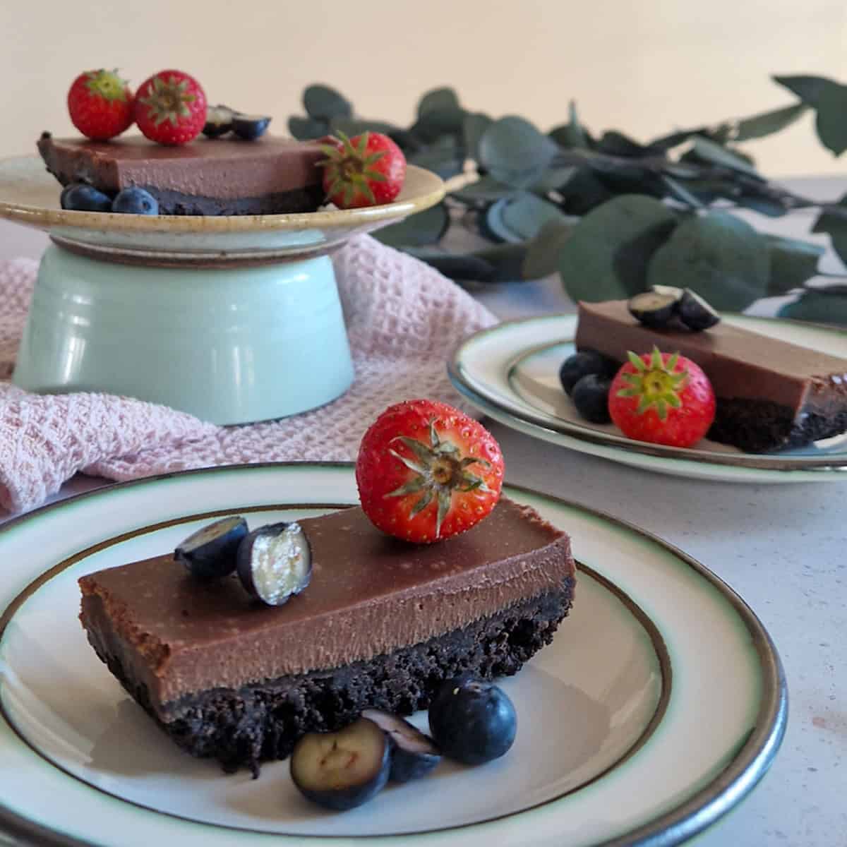 Oreo ganache cake on a small plate. The rest of the no bake cake is visible in the background. The cake is topped with fresh strawberries.