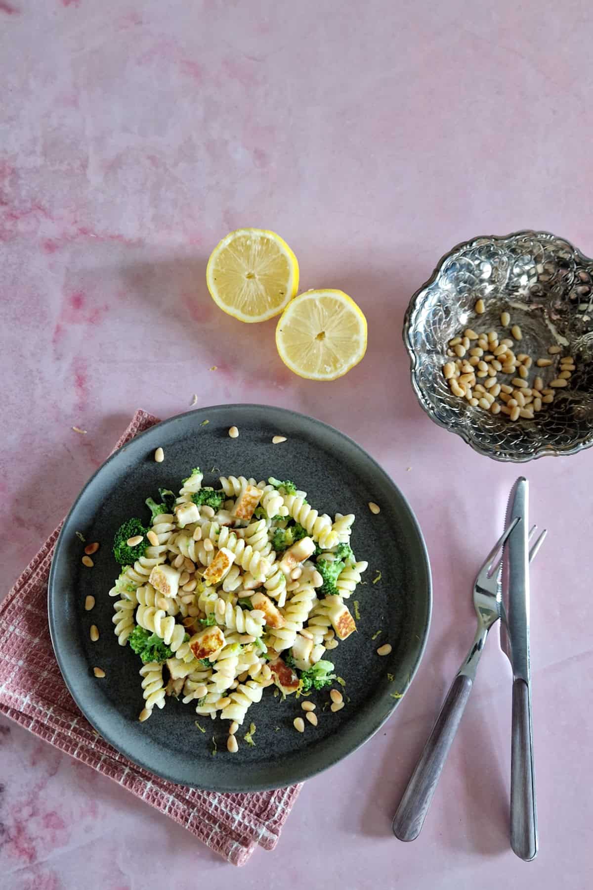 A gray plate filled with Boursin pasta. Next to the plate are a halved lemon and a bowl of pine nuts.
