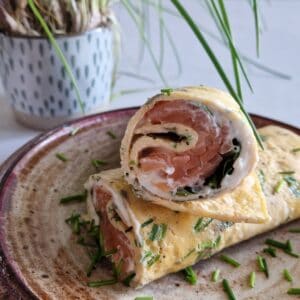 A smoked salmon omelette with herbs, cut in half and served on a plate.