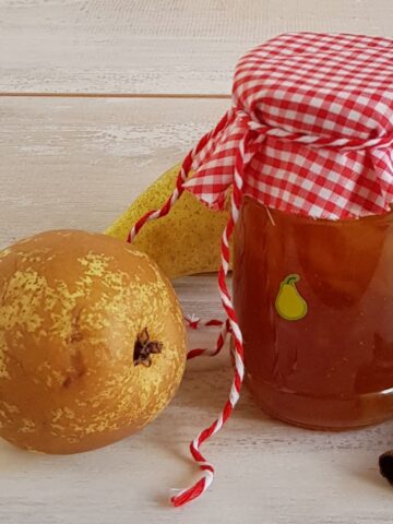 A glass jar filled with pear ginger jam. There are two pears next to the jar.