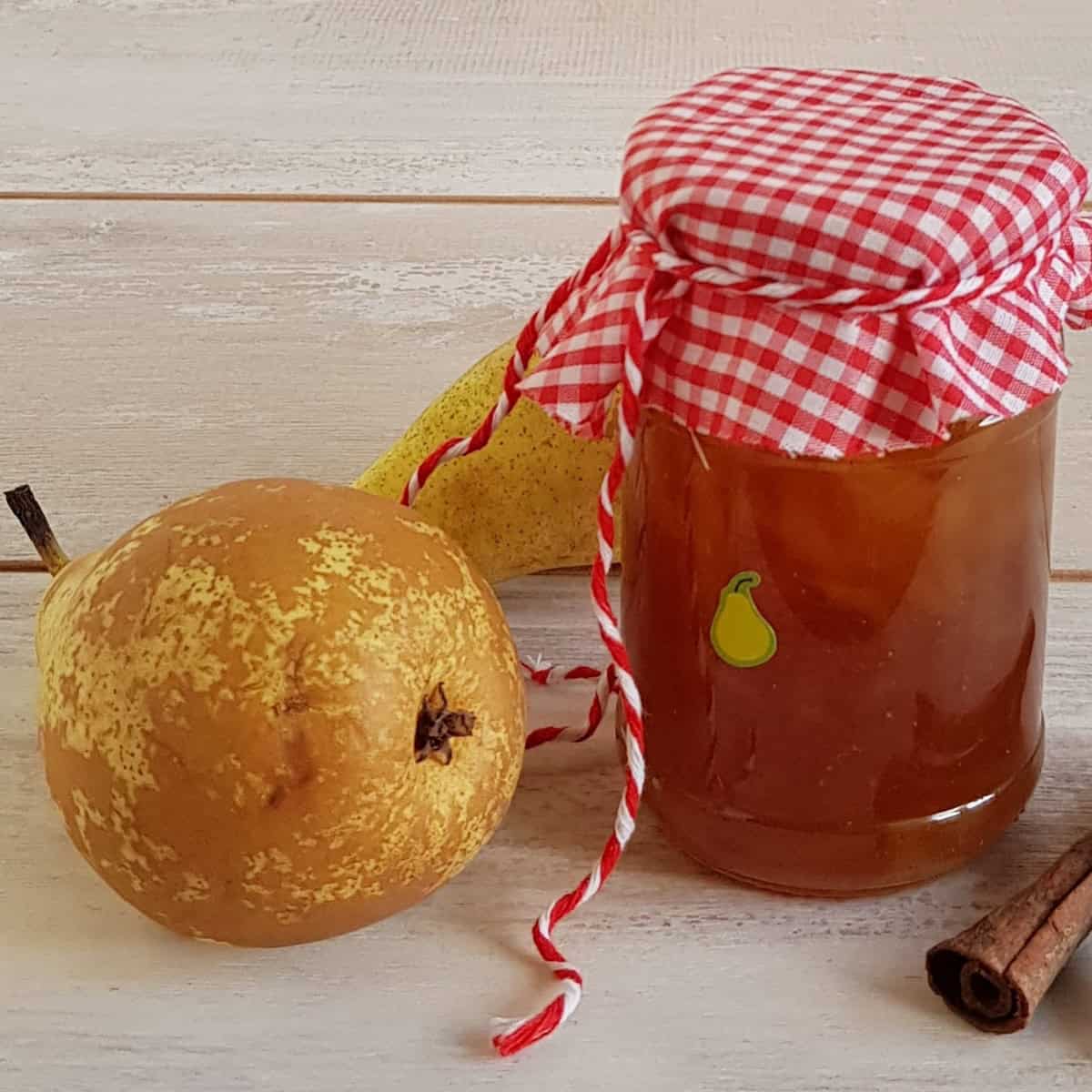 A glass jar filled with pear ginger jam. There are two pears next to the jar.