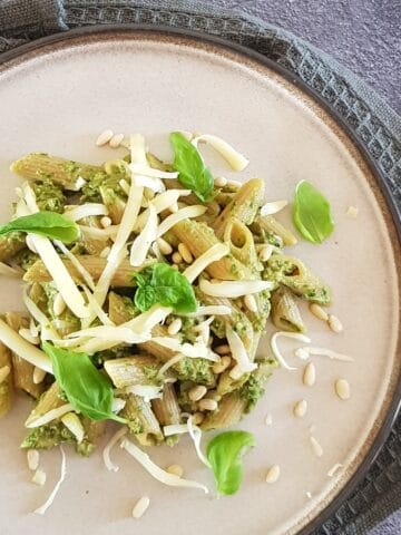 A plate filled with swiss chard pasta, garnished with shavings of Parmesan cheese.