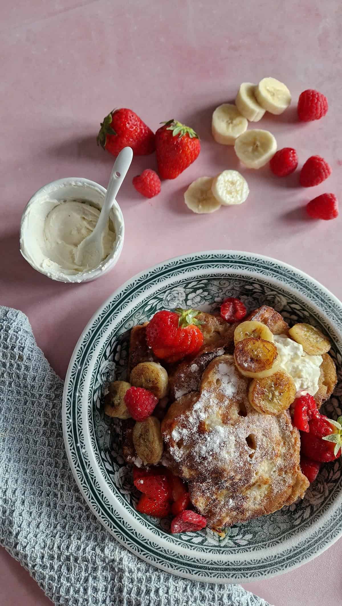 A plate of brioche French toast, with fresh strawberries, bananas and a vanilla mascarpone topping.