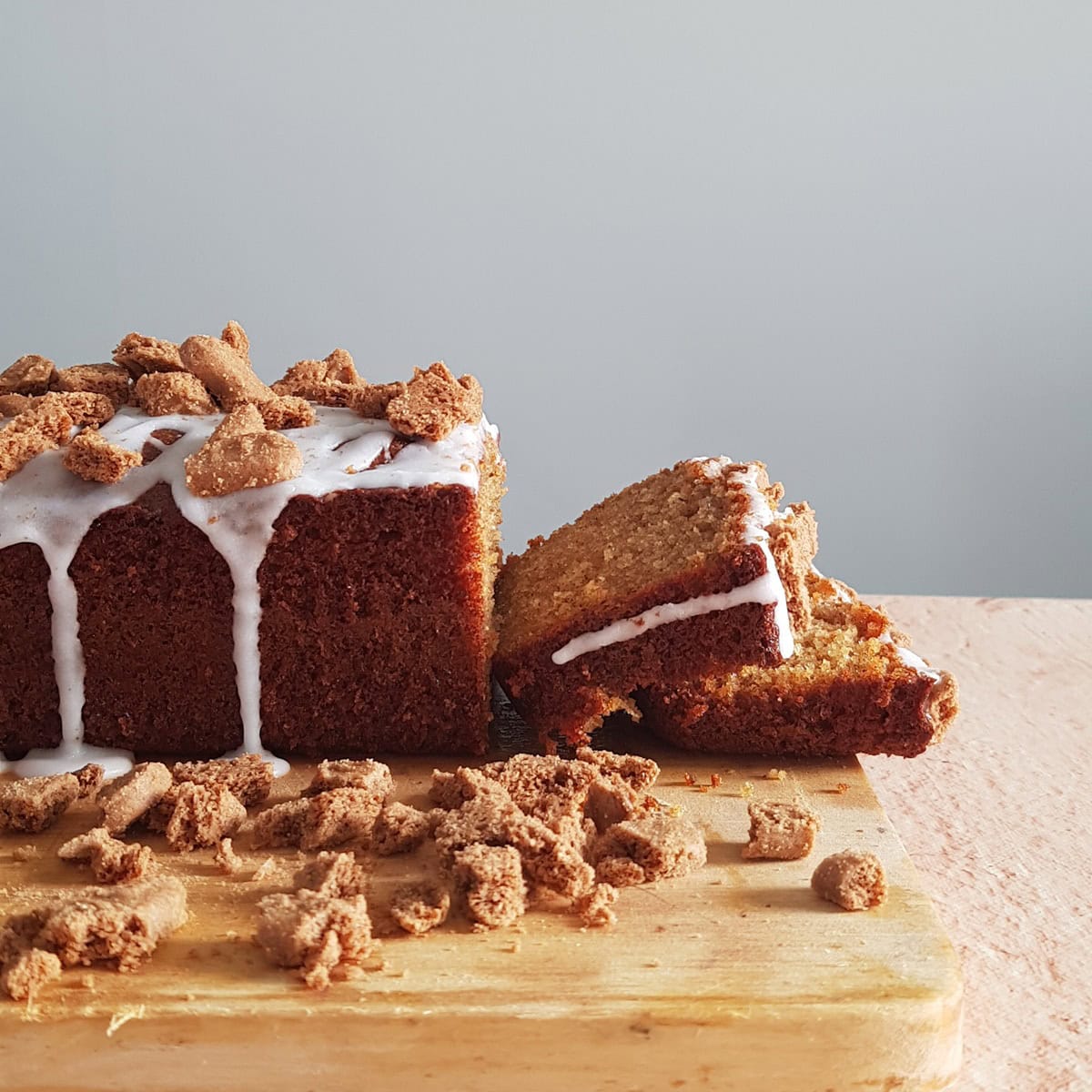 A cinnamon loaf cake with a few slices cut off. The cinnamon cake is covered with a white frosting and a cookie crumble topping.