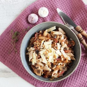 A bowl filled with bacon and mushroom pasta, generously garnished with shaved Parmesan flakes.
