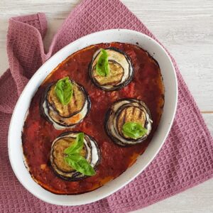 A casserolle with four eggplant stacks: stacks of eggplant and mozzarella in a tomato sauce.