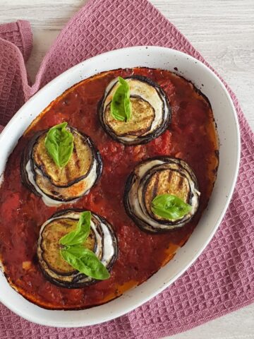 A casserolle with four eggplant stacks: stacks of eggplant and mozzarella in a tomato sauce.