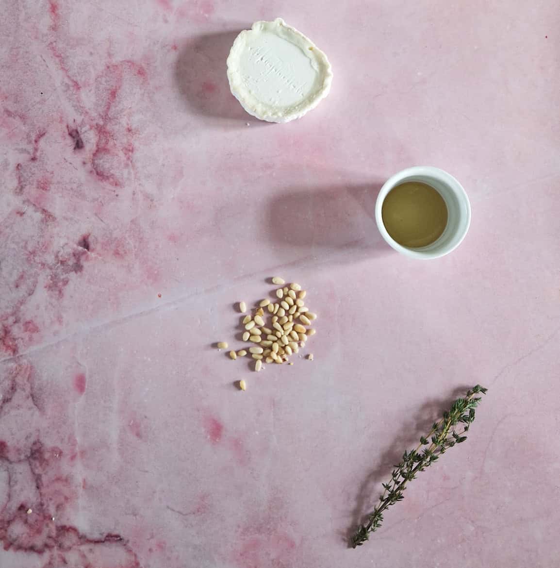 The ingredients to make baked goats cheese, layed out on a pink marble backdrop.