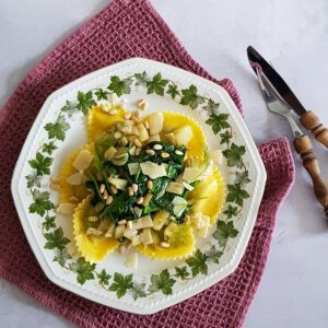 A plate filled with ravioli with spinach, fennel, shaved parmesan cheese and pine nuts.