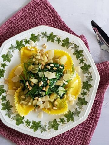 A plate filled with ravioli with spinach, fennel, shaved parmesan cheese and pine nuts.