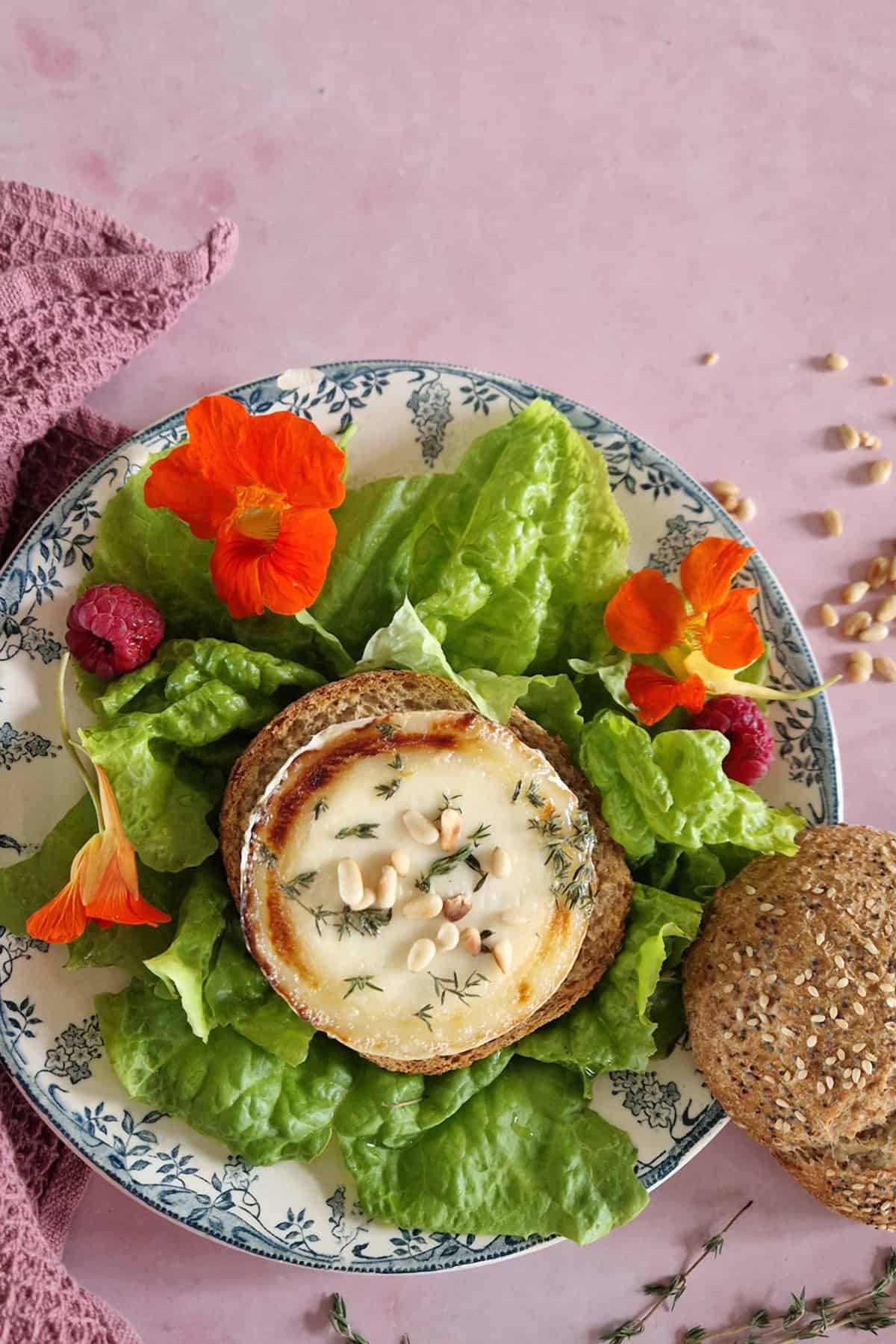 A warm goat cheese appetizer with a green salad and a piece of wholegrain bread.