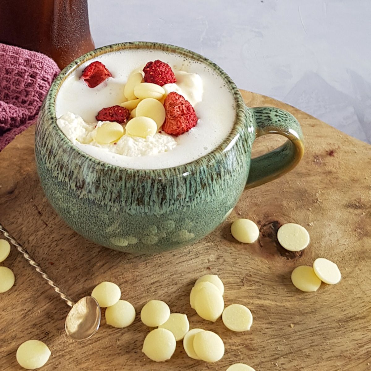 A mug of white chocolate milk, served with white chocolate drops and freeze dried strawberries.
