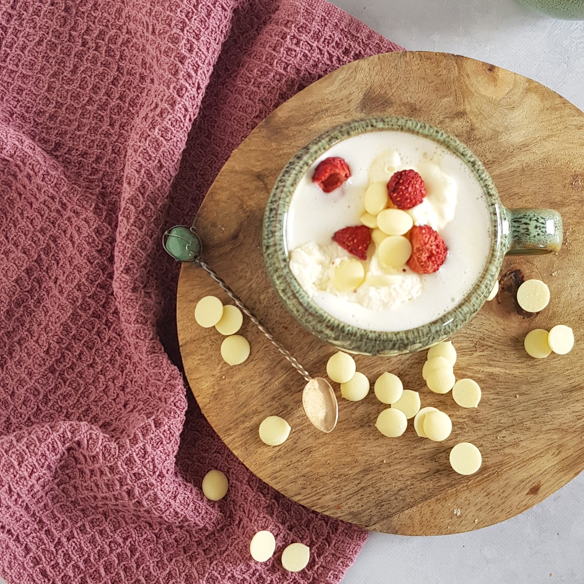Top view of a mug filled with white hot chocolate. The drink is garnished with whipped cream, white chocolate and strawberries (freeze-dried).