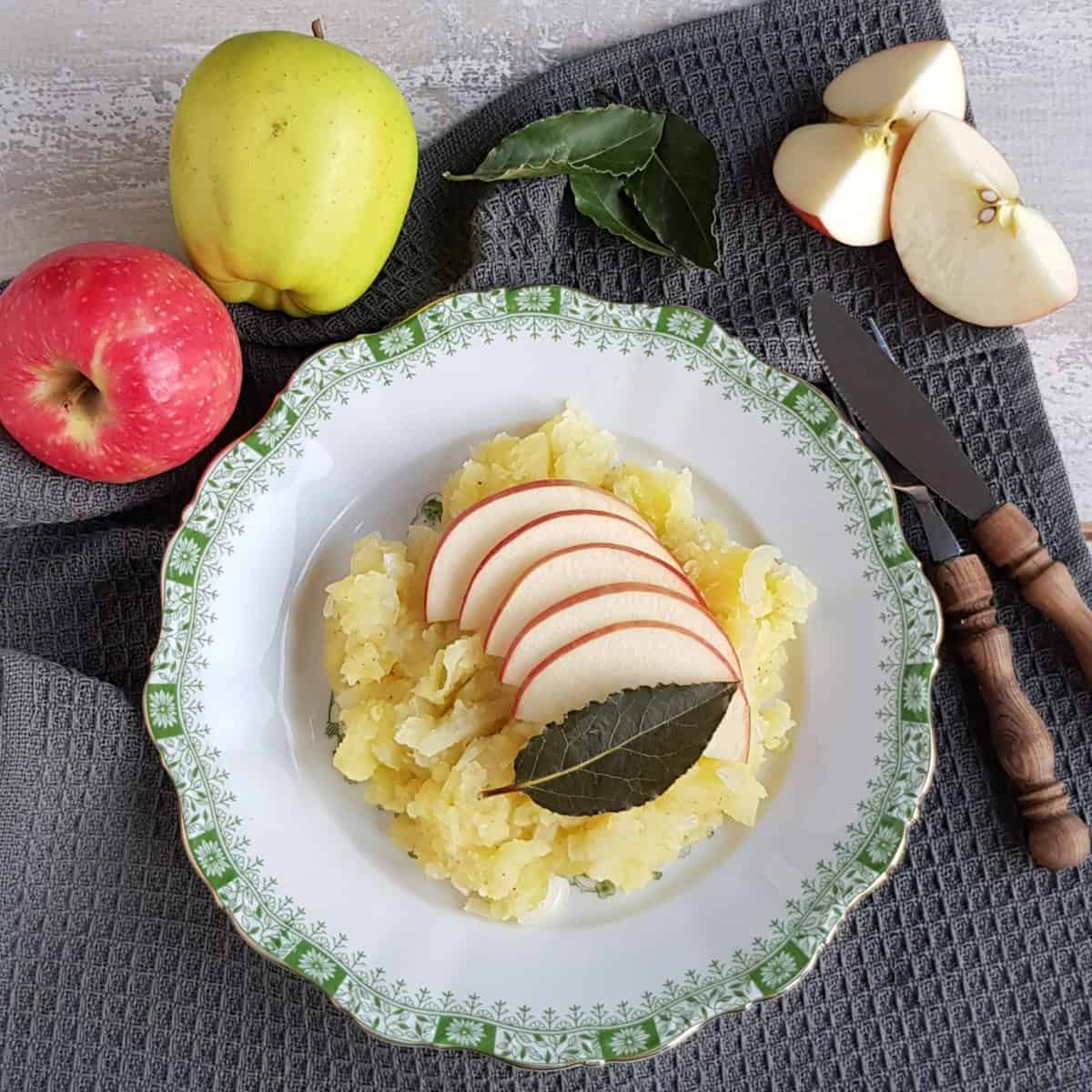 A plate filled with Hete Bliksem (Dutch Apple Mashed Potatoes). The dish is garnished with a bay leaf.