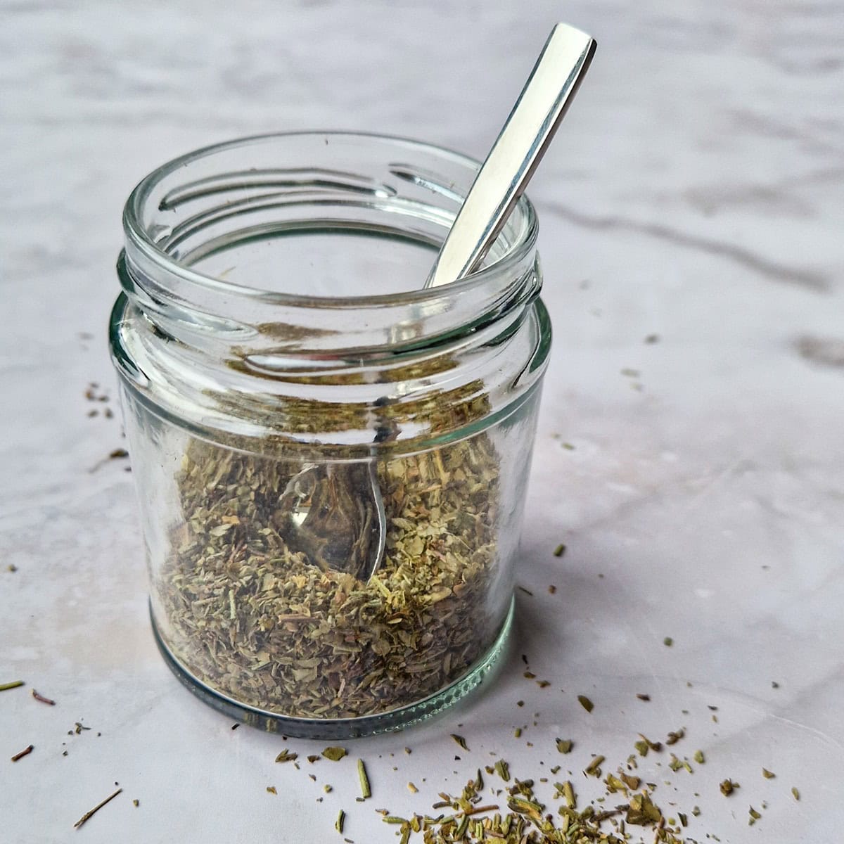 A glass jar filled with homemade Italian herb seasoning.