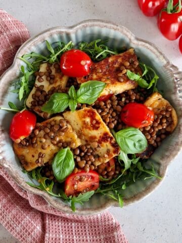Lentil bowl with halloumi, fresh halved cherry tomatoes and fresh basil.