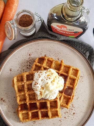 A pile of carrot waffles, served with maple syrup, yoghurt and cinnamon.