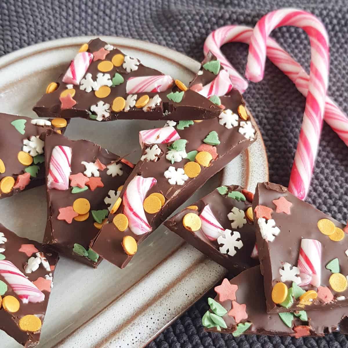 A pile of peppermint chocolate bark. The bark is broken into pieces. There are two candy canes on the side.
