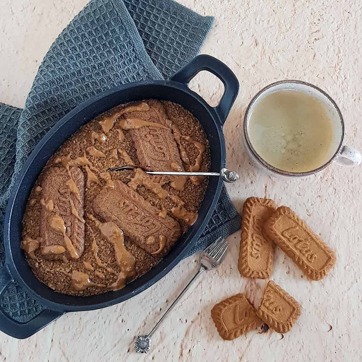 Biscoff baked oats, straight from the oven. There are a few biscoff cookies and a cup of coffee next to the breakfast.