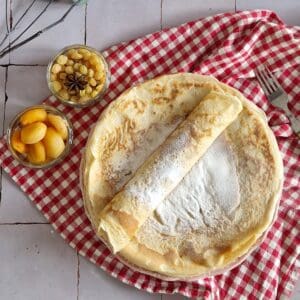A pile of Dutch Pannenkoeken. The top pannenkoek is rolled up and dusted with icing sugar.