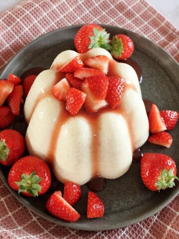 A close-up of a Dutch Griesmeelpudding, served with strawberry sauce and fresh strawberries.