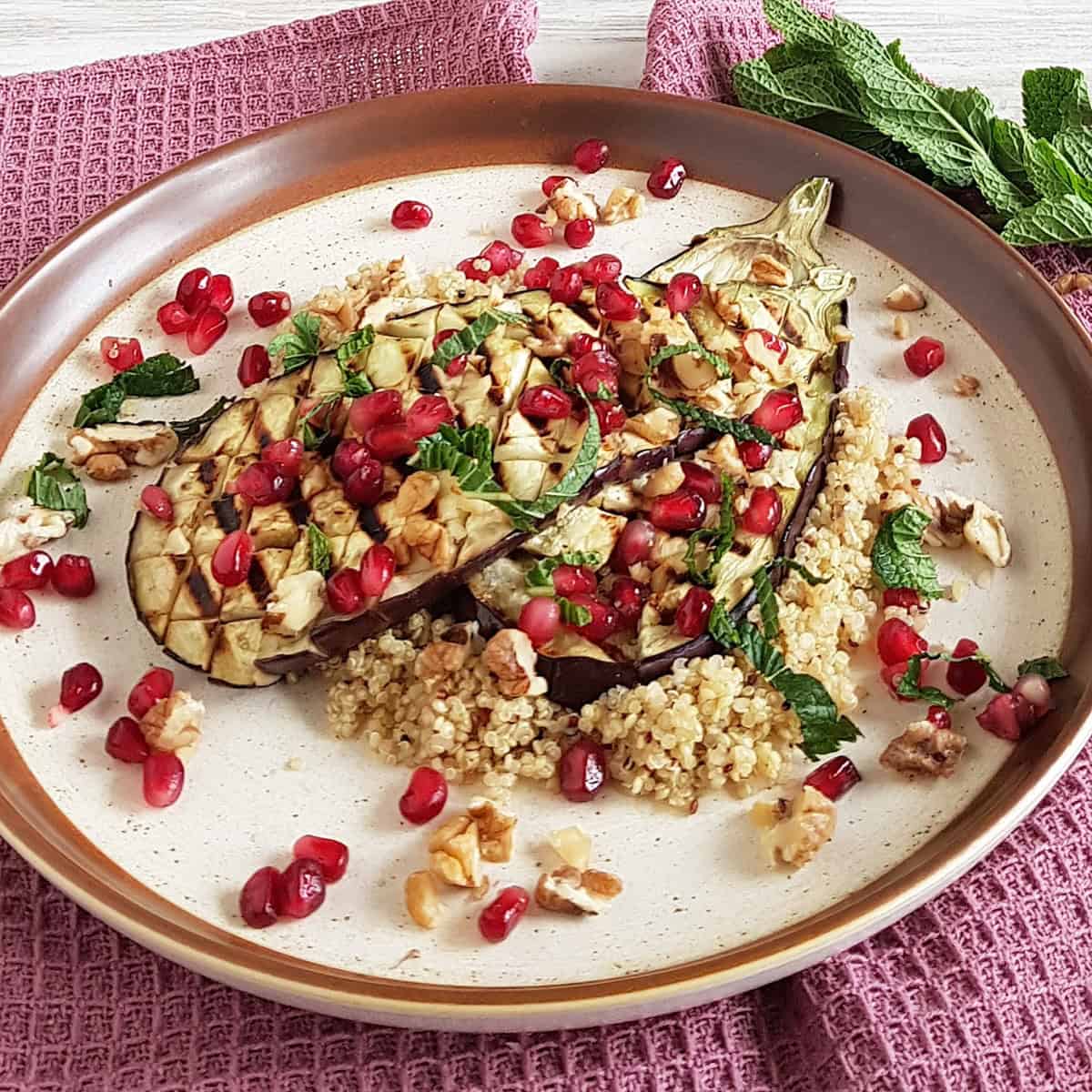 Close-up of charred eggplant couscous, sprinkled with pomegrenate seeds and fresh mint.