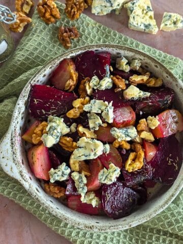 A bowl with roasted beetroot salad, topped with blue cheese and walnuts.