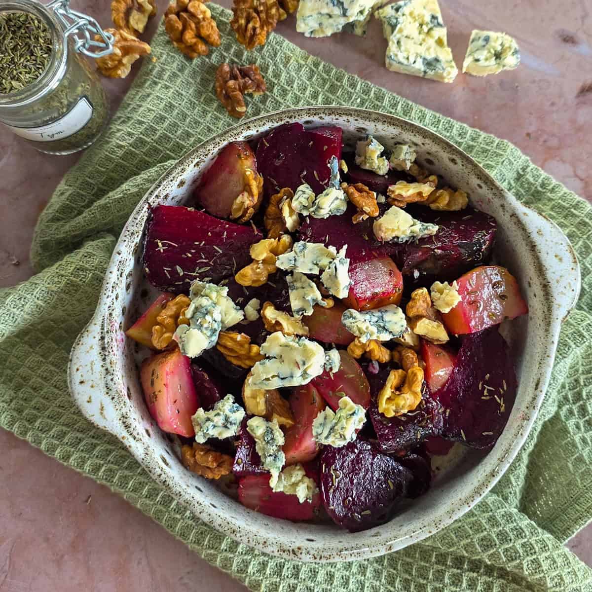 A bowl with roasted beetroot salad, topped with blue cheese and walnuts.
